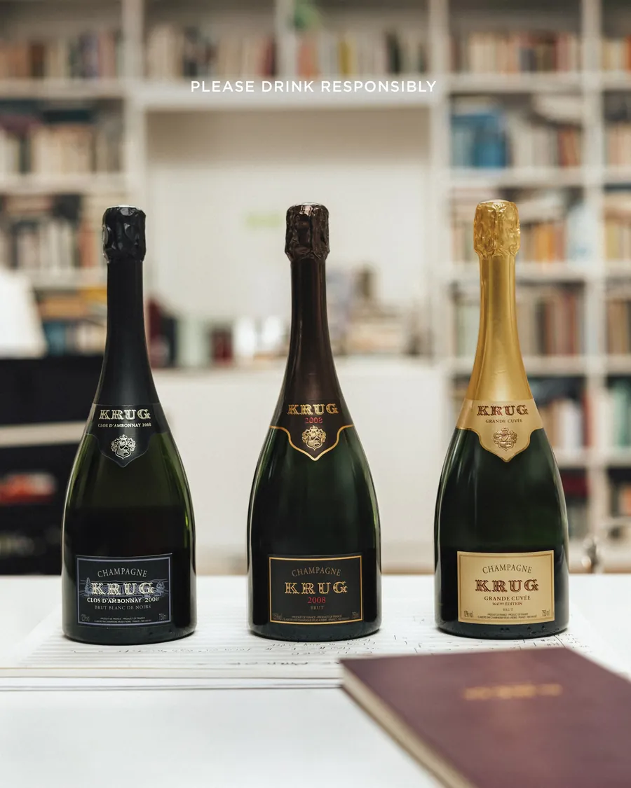 Three bottles of Krug champagne in front of a bookshelf
